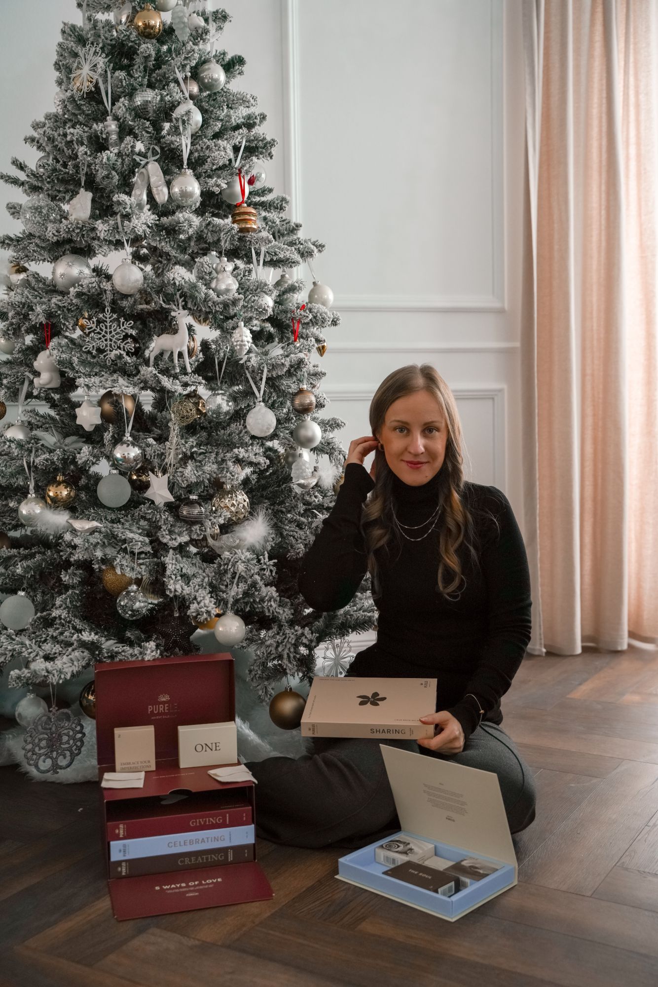 Priscilla Schürch sitzt vor einem weiß geflockten Weihnachtsbaum mit geöffneten Adventskalender-Boxen von PURELEI