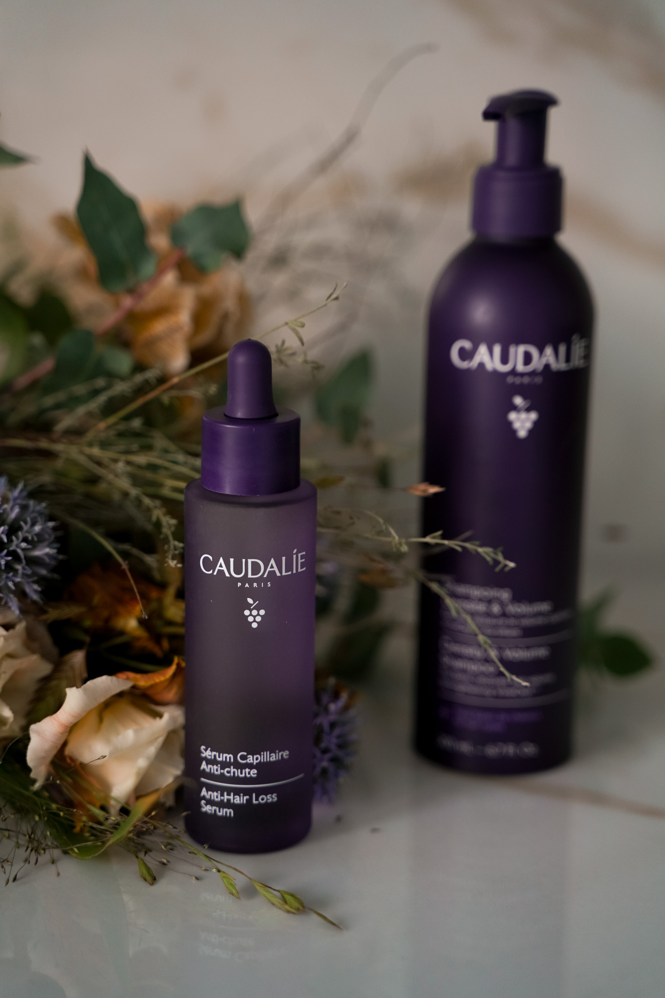 Caudalie Anti-Hair Loss Serum und Shampoo vor Trockenblumen